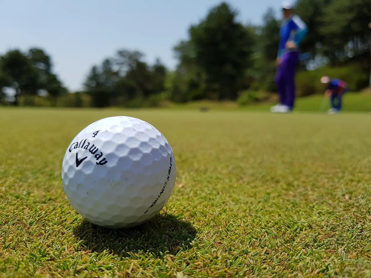 Golfbold på putting green med to golfspillere i baggrunden